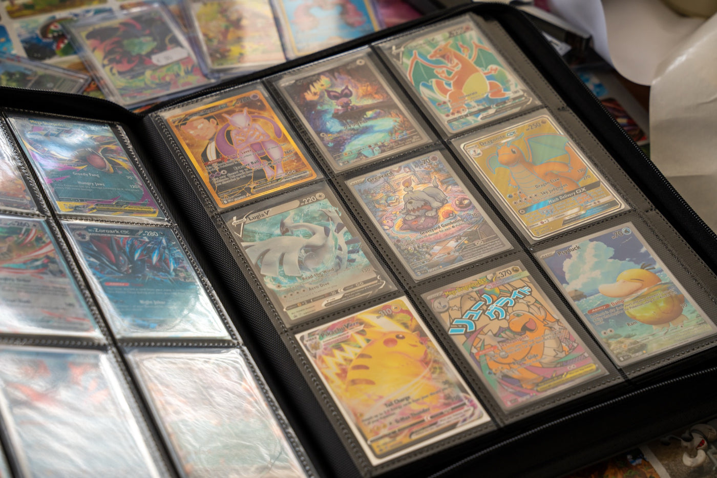 Een opengeslagen verzamelmap met Pokemon-kaarten in sleeves, met losse kaarten eromheen op tafel